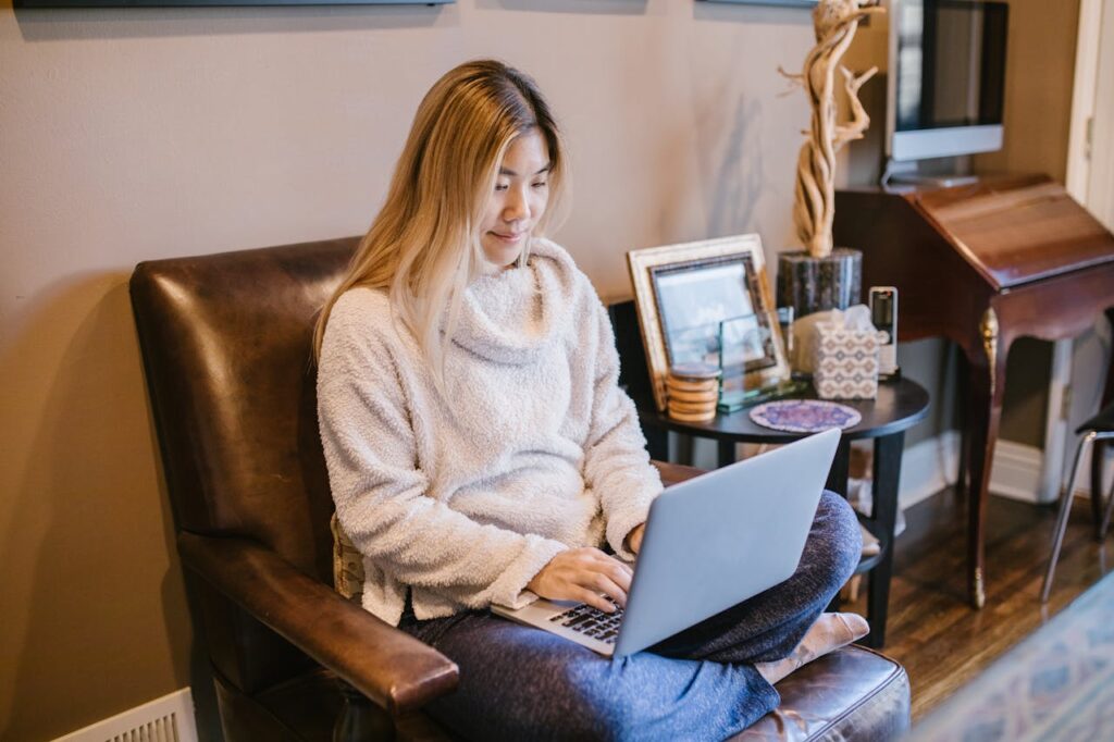 Woman seated on a chair using a laptop, enjoying a cozy home office environment.